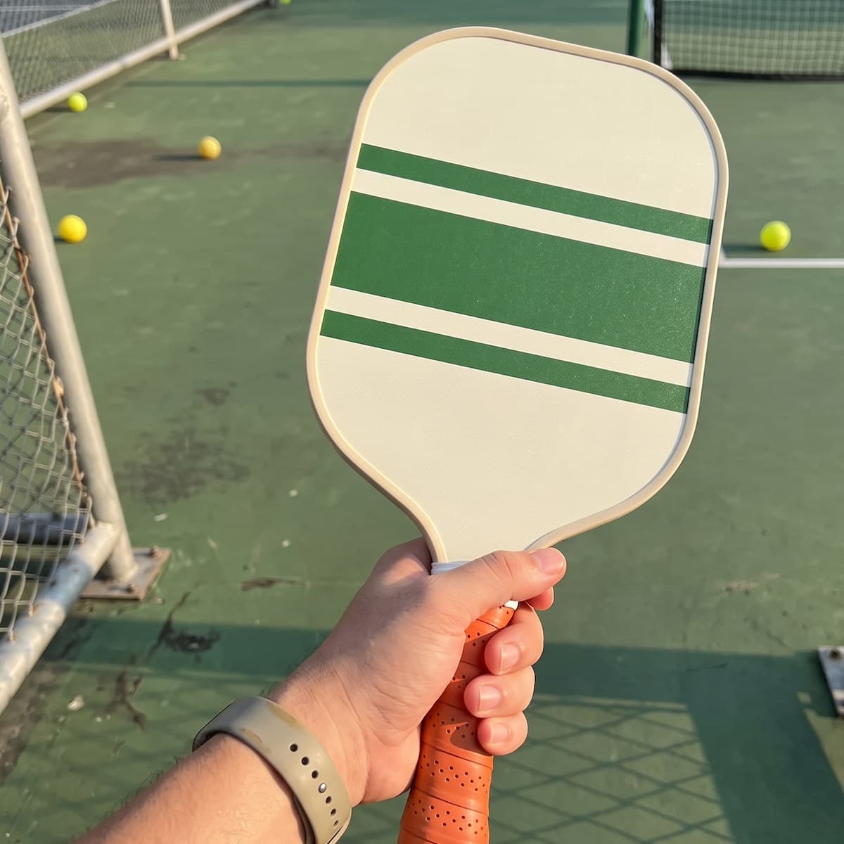 The green-striped Picklr paddle held in one hand on an outdoor court in late afternoon light